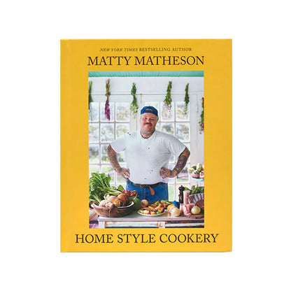 Home Style Cookery book cover featuring a bright yellow border, with a professional chef in a kitchen setting surrounded by fresh ingredients and hanging herbs. Rustic wooden table displays prepared dishes and cooking ingredients against a sunlit window backdrop.