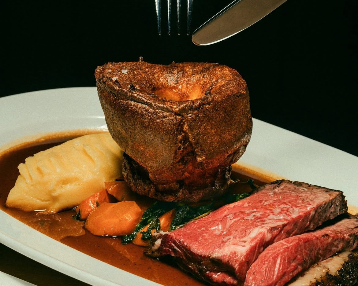 Plated dinner with beef, vegetables, and Yorkshire pudding on a black background