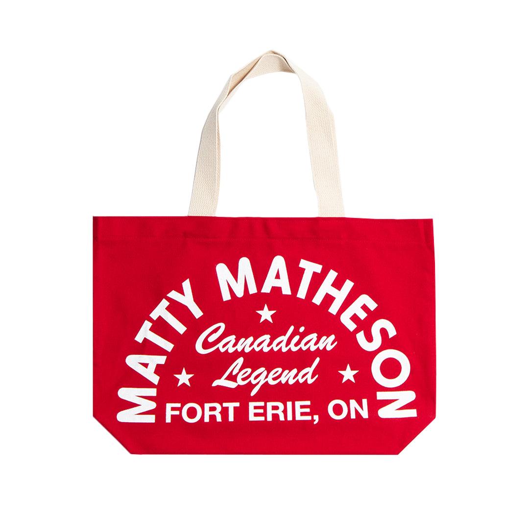Chef Matty Matheson Canadian Legend Tote Bag in vibrant red cotton canvas featuring white curved text design and star accents on one side, with natural beige handles. Shows 'Canadian Legend' text and Fort Erie, ON location against bold red background.