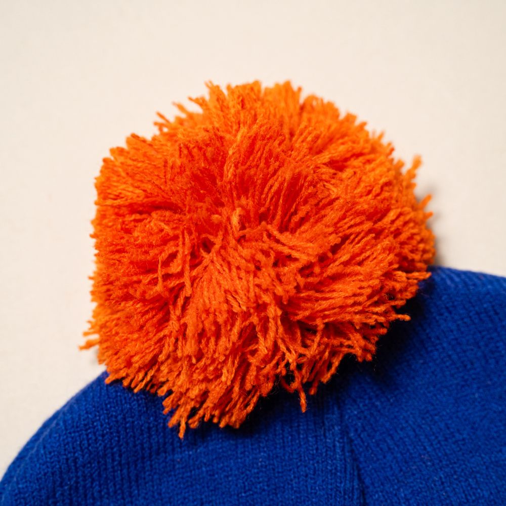 Blue beanie with an orange pom-pom on a beige background