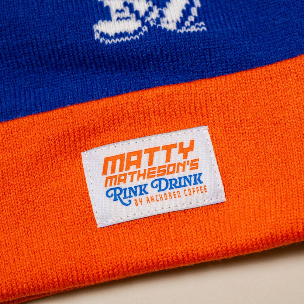 Blue and orange beanie with a label reading 'Matty Matheson's Rink Drink by Anchored Coffee'.