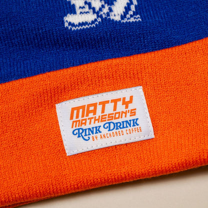 Blue and orange beanie with a label reading 'Matty Matheson's Rink Drink by Anchored Coffee'.